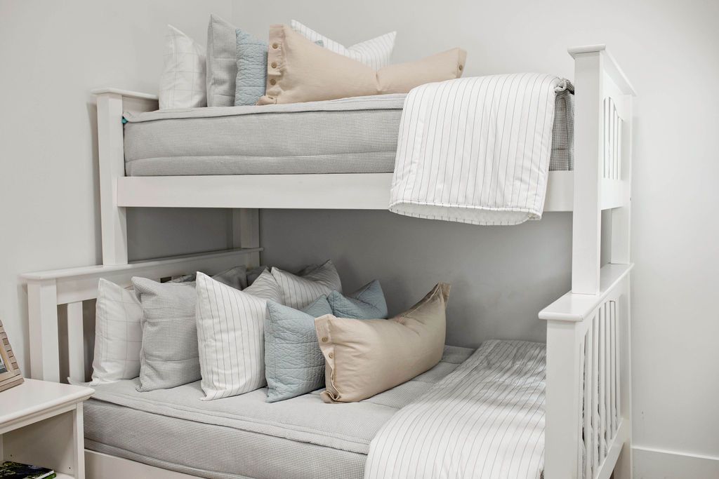 Twin bunk bed with Light gray zipper bedding with white and gray pillowcases and shams. Decorated with light blue pillows, cream lumbar pillow, and white pin stripe blanket