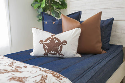 A close up view of a twin bed made with denim blue zipper bedding and neutral and brown and white western theme pattern pillows and blanket.