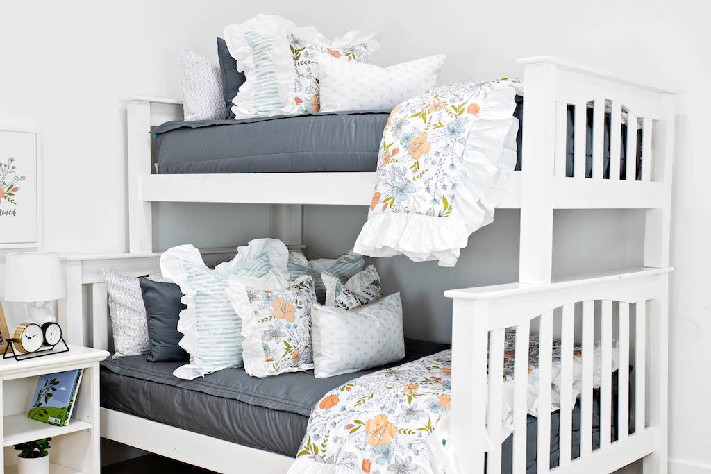 bunk bed with Gray zipper bedding with white and blue striped euro with ruffle along the edge, floral printed pillow, white lumbar with small gray floral design and floral printed blanket with white ruffle along the edge