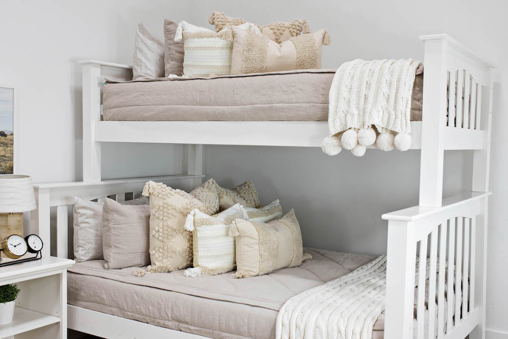 bunk bed with Tan textured zipper bedding dark creamy textured euro, a cream and tan woven textured pillow and a textured dark creamy lumbar with tassels with an off white braided throw with pom poms along the edge
