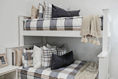 A standard bunk bed with both bunks made with tan, charcoal, and cream plaid zipper bedding and neutral and leather pillows and blankets.