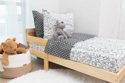A toddler bed made with charcoal and white pattern dogs kids zipper bedding and a basket of stuffed animals beside it.