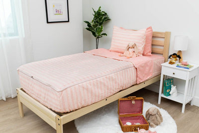 A twin bed made with pink ballet shoes kids zipper bedding, a nightstand beside it with books on the shelf and toys scattered on the floor.