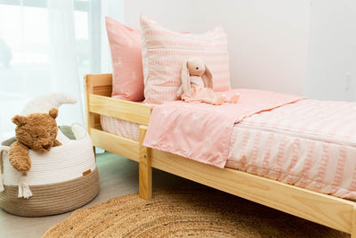 A toddler bed made with pink ballet shoes kids zipper bedding and a basket of stuffed animals beside it.