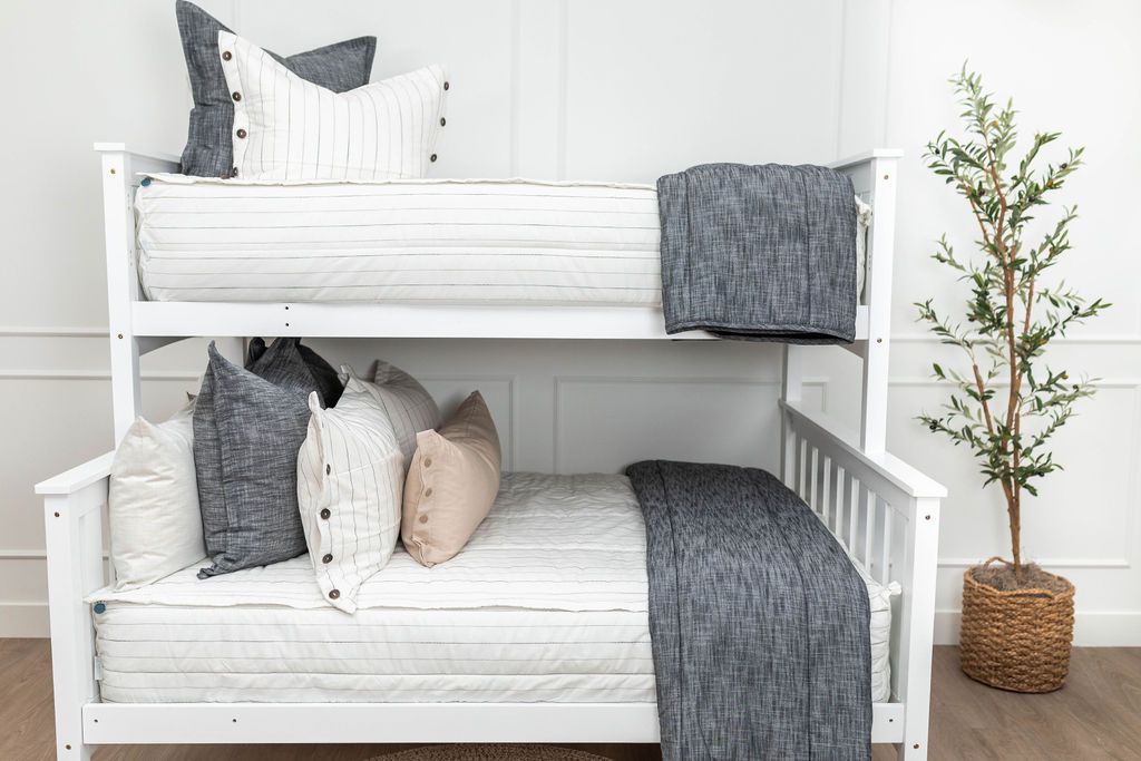 A standard bunk bed with both bunks made with white and pinstripes zipper bedding and neutral and dark charcoal gray pillows and blankets.