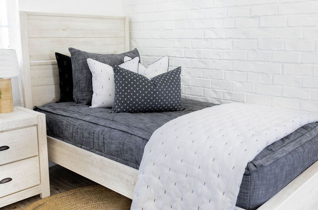 White blanket with black edge and small black lines on charcoal gray zipper bedding with matching pillows