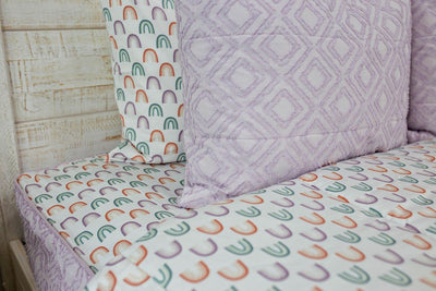 Up close shot of purple textured pillow sham and white sheets with purple, orange and green rainbows