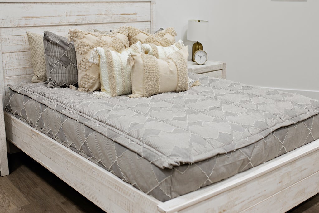 Queen bed with Taupe bedding with textured zig zag design dark creamy textured euro, a cream and tan woven textured pillow and a textured dark creamy lumbar with tassels