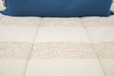 Close up showing pattern and texture of tan zipper bedding with blue lumbar pillow