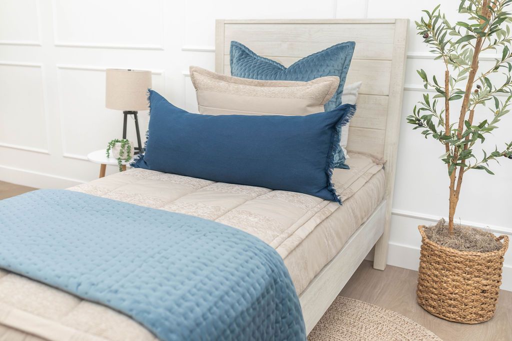 Tan zipper bedding styled with tan, blue and white pillows and blue blanket