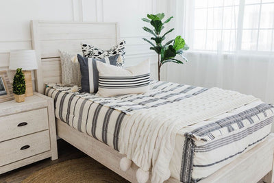 twin bed with cream and black woven striped bedding, a white and black euro pillow, a medium black and cream textured pillow, a cream and black striped lumbar pillow, a cream cable-knit throw at the foot of the bed.