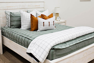 Queen bed with Green striped bedding with white and black grid euro, faux leather pillows, white and black striped lumbar with faux lather buckles and white and black grid pattered blanket