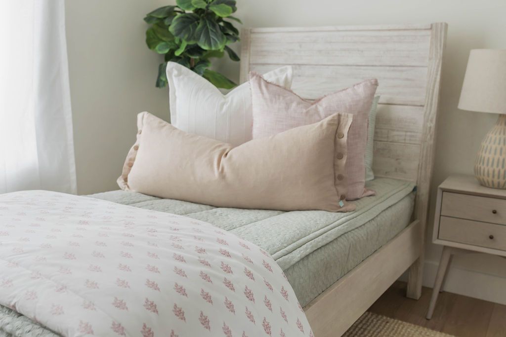 Sage green zipper bedding with sage green pillow cases and shams. Decorated with white and pink pillows and white and pink blanket. Cream lumbar pillow