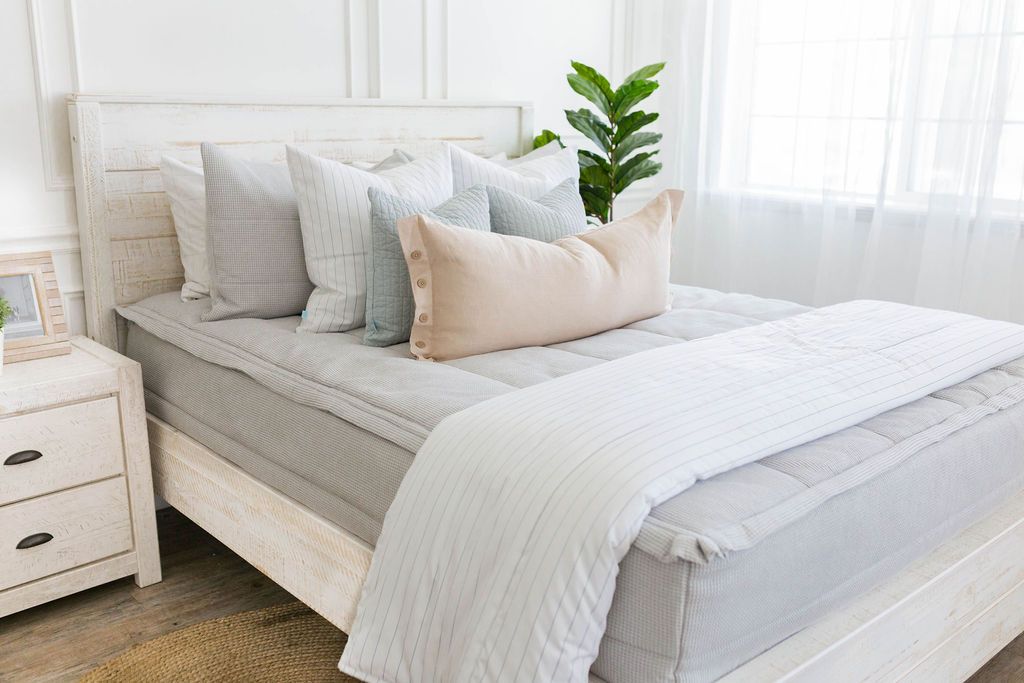 Light gray zipper bedding with white and gray pillowcases and shams. Decorated with white and light blue pillows, cream lumbar pillow, and white pin stripped blanket