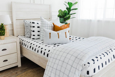 twin bed with White bedding with black dashed lines and white and black grid euro, faux leather pillows, white and black striped lumbar with faux lather buckles and white and black grid pattered blanket