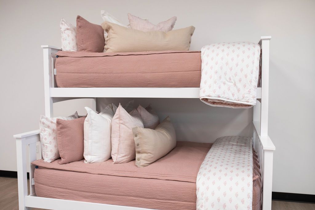 A standard bunk bed with both bunks made with woven pink zipper bedding and neutral and pink pattern pillows and blankets.
