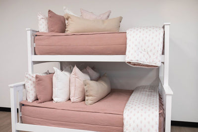 A standard bunk bed with both bunks made with woven pink zipper bedding and neutral and pink pattern pillows and blankets.