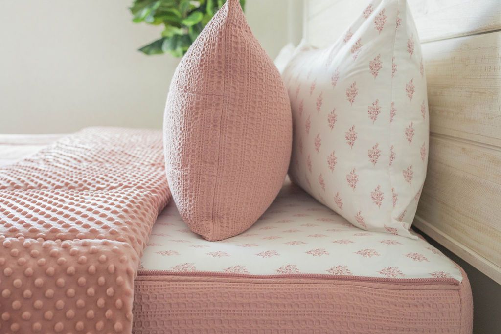 A close up side view of a bed made with woven pink zipper bedding with the top unzipped halfway down the bed and the comforter folded down.
