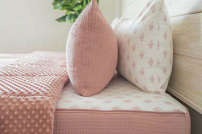 A close up side view of a bed made with woven pink zipper bedding with the top unzipped halfway down the bed and the comforter folded down.