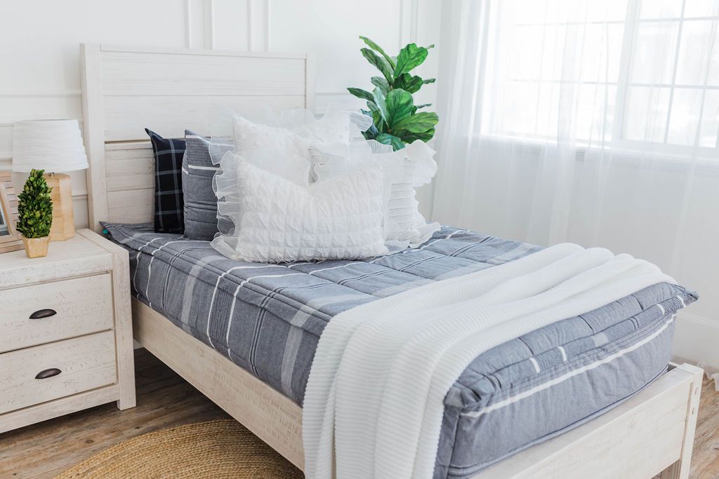 twin bed with Deep navy woven stripe bedding white ruffle polka dot euros,  ruffle gray/blue textured pillows, white ruffle textured lumbar, and a textured white throw with braided tassels