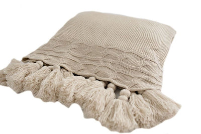 A folded tan woven throw blanket with tassels on a white background.