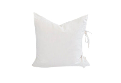 A white cream linen pillow with ties on the side.