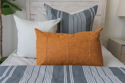 A close up of a twin bed made with light gray waffle textured zipper bedding and neutral and leather pillows and a matching striped blanket.