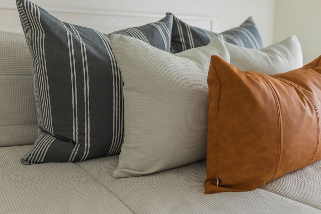 A close up view of a bed made with light gray waffle textured zipper bedding and neutral, leather, and gray striped pillows.