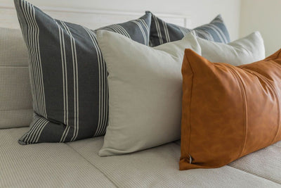 A close up view of a bed made with light gray waffle textured zipper bedding and neutral, leather, and gray striped pillows.