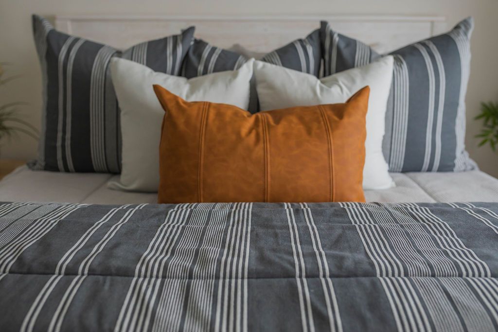 A close up of a bed made with light gray waffle textured zipper bedding and neutral and leather pillows and a matching striped blanket.