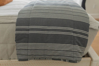 A close up size view of a bed made with light gray waffle textured zipper bedding and a charcoal gray striped blanket folded over the end of the bed.