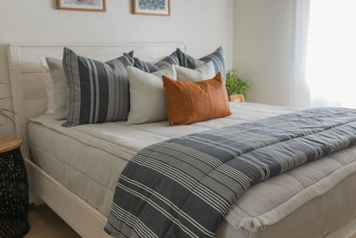 A bed made with light gray waffle textured zipper bedding and gray striped pillows and blanket.