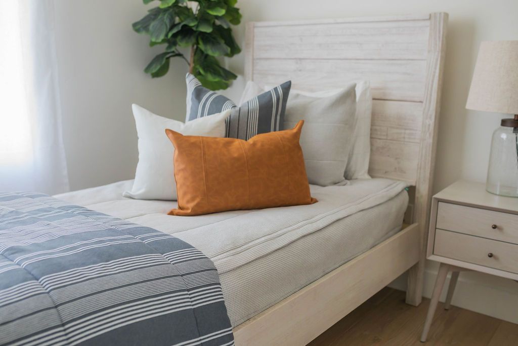 A twin bed made with light gray waffle textured zipper bedding and gray striped neutral pillows and matching blanket.