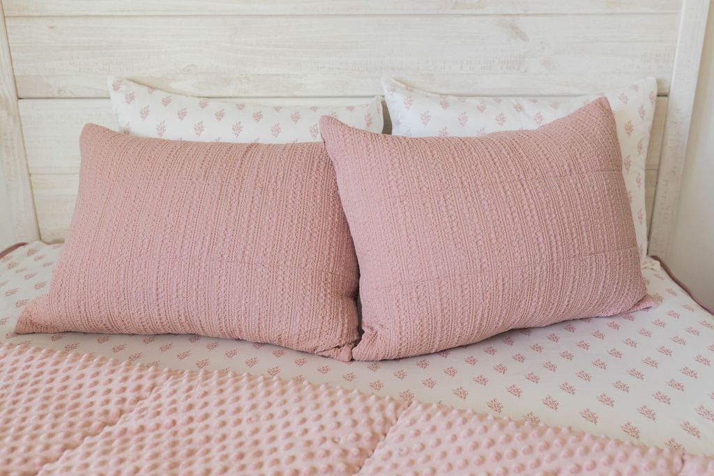 A bed made with pink woven zipper bedding with the comforter pulled back and pillows on top of the bed.