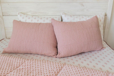 A bed made with pink woven zipper bedding with the comforter pulled back and pillows on top of the bed.