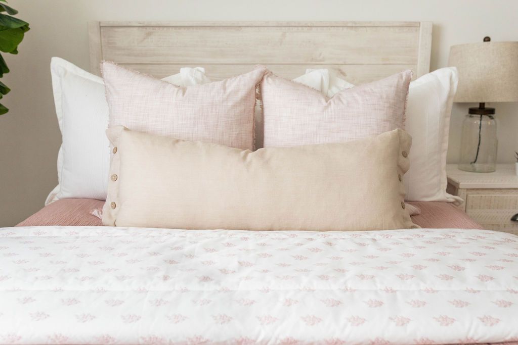 A close up view of a bed made with woven pink zipper bedding and an assortment of neutral and light pink throw pillows and blanket.