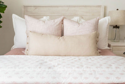 A close up view of a bed made with woven pink zipper bedding and an assortment of neutral and light pink throw pillows and blanket.