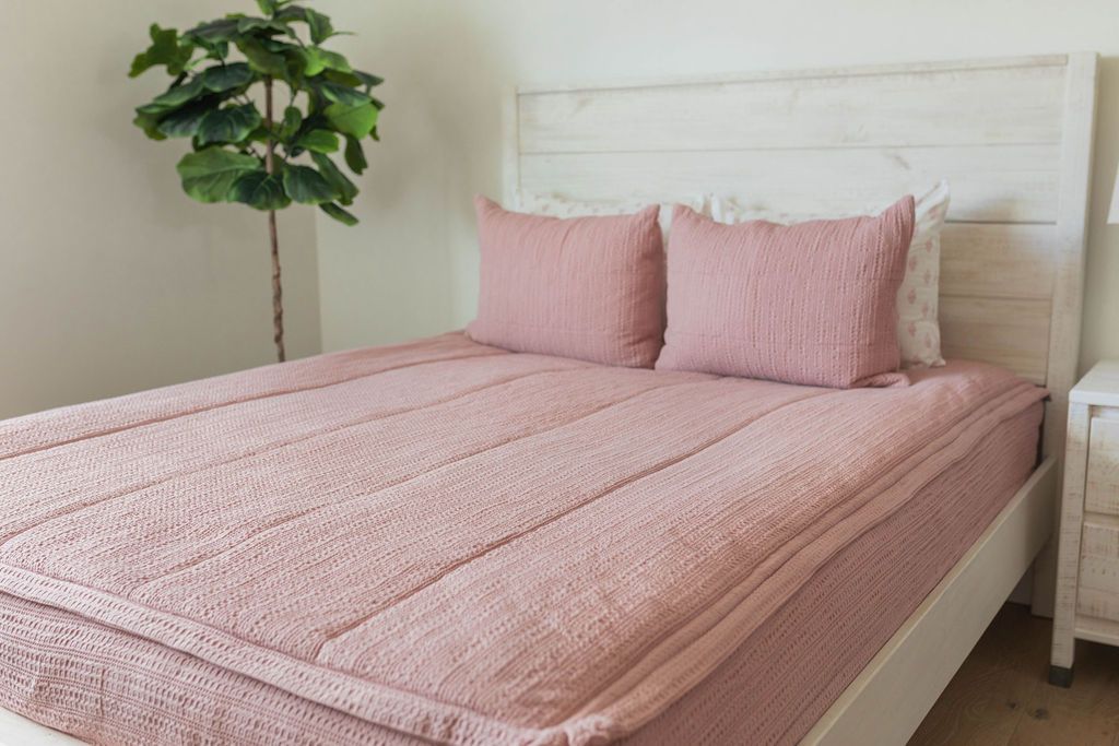 A bed made with pink woven zipper bedding and matching pillows.