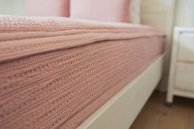 A close up side view of a bed made with woven pink zipper bedding.
