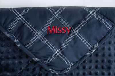 A navy blue plaid children's blanket with red custom personalized embroidery. 
