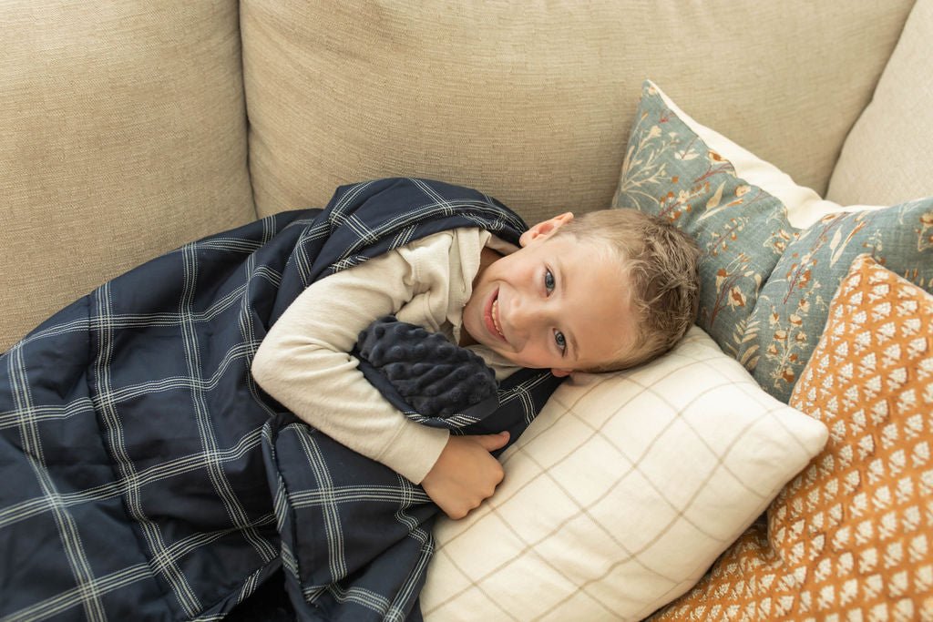 A child smiling on couch cuddling with a navy blue plaid pattern children&