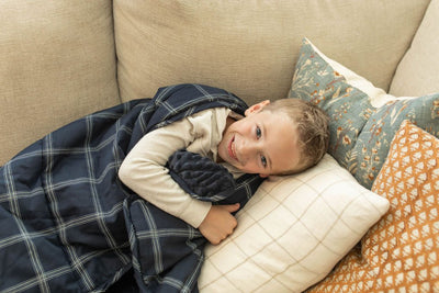 A child smiling on couch cuddling with a navy blue plaid pattern children's blanket.