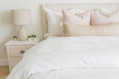 A bed made with a white woven textured zipper duvet folded half way down the bed and adorned with neutral and light pink pillows.