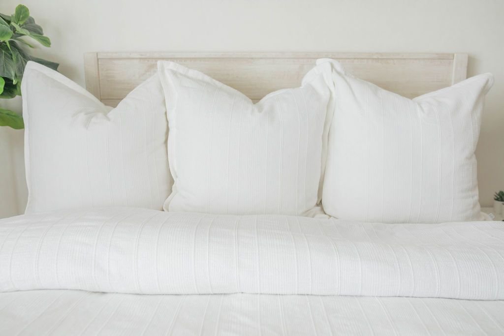 A bed made with a white woven textured zipper duvet folded partially down the bed and adorned with matching white pillows.