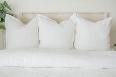 A bed made with a white woven textured zipper duvet folded partially down the bed and adorned with matching white pillows.
