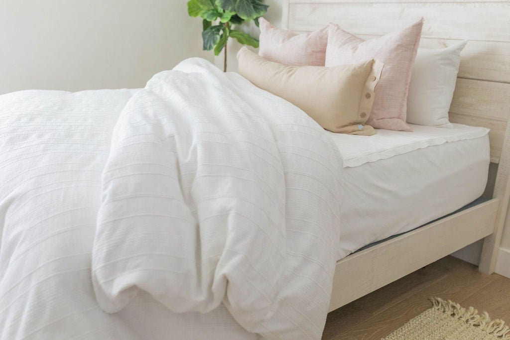 A twin bed made with white zipper sheets and a white textured zipper duvet partially folded half way down the bed and adorned with neutral and light pink pillows.