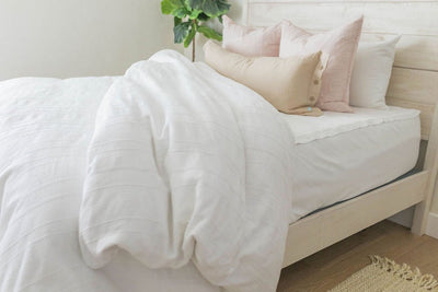 A twin bed made with white zipper sheets and a white textured zipper duvet partially folded half way down the bed and adorned with neutral and light pink pillows.