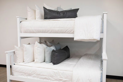 A standard bunk bed with both bunks made with white woven plaid zipper bedding and neutral and striped pillows and blankets.