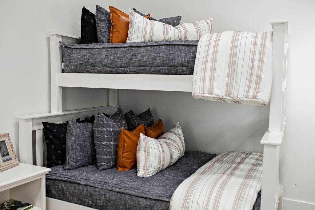A standard bunk bed with both bunks made with dark charcoal gray zipper bedding and neutral and striped pattern pillows and blankets.