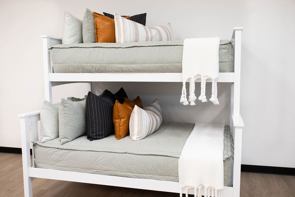 A standard bunk bed with both bunks made with soft green zipper bedding and neutral and leather throw pillows and blankets.